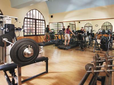 Großer Fitnessraum mit Gewichten, Geräten und drei Personen beim Training.