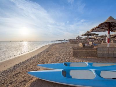 Catamarán azul en la playa con áreas de descanso y sombrillas al atardecer.