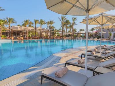 Groot zwembad met ligstoelen en parasols in een tropisch hotelresort.