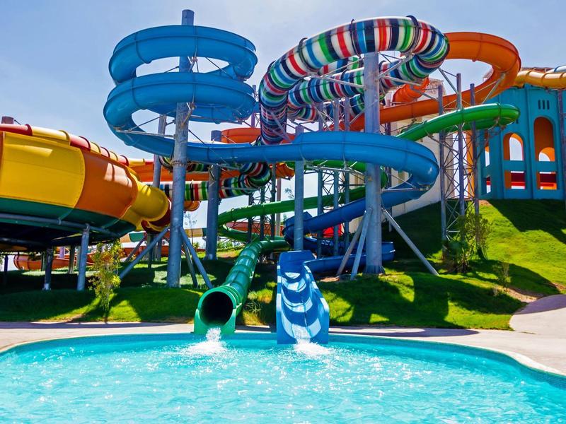 Kleurige glijbanen in een waterpark die uitkomen in een helderblauw zwembad onder een zonnige hemel.