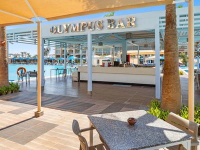 Buiten bar met tafels onder een gele luifel bij water en palmbomen.