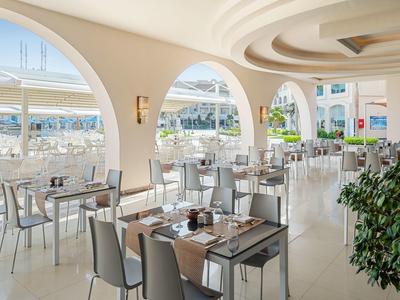 Salle de restaurant d'hôtel avec grandes arches et vue sur la mer.