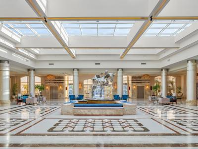 Hall d'un hôtel luxueux avec grande fontaine centrale sous plafond vitré.
