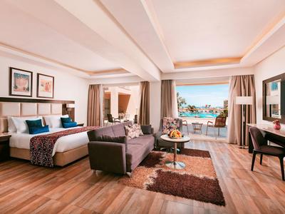 Habitación de hotel espaciosa con cama doble, área de estar y vista a una terraza con vista al mar.