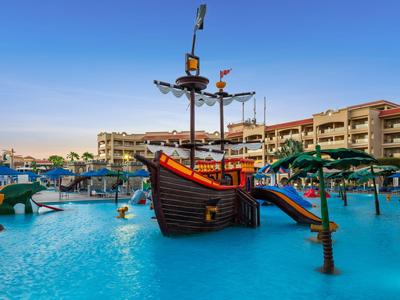 Parque acuático con un barco pirata para juegos en una piscina de hotel al atardecer.