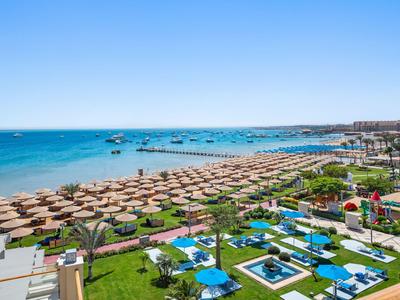 Widok na plażę z parasolami i basenami w kompleksie hotelowym nad morzem.