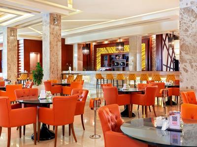 Salón luminoso del hotel con sillas naranjas y mesas redondas, iluminación cálida.