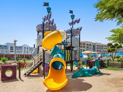 Colorido parque infantil con tobogán en el jardín de un hotel bajo cielo despejado y rodeado de edificios.