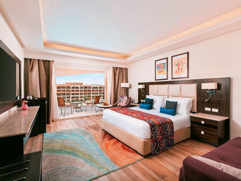 Habitación de hotel moderna con cama grande, televisión, balcón con vista y decoración elegante.