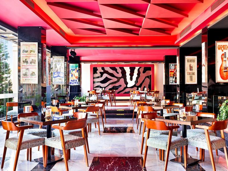 Restaurante moderno con elementos rojos en el techo, mesas de madera y sillas en un ambiente elegante.