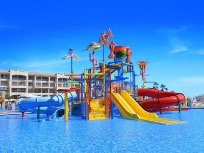 Wasserspielplatz mit bunten Rutschen und Wasserfontänen in einem Hotelpool bei klarem Himmel.