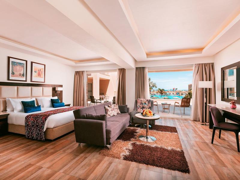 Spacious hotel room with king bed, seating area, desk, and ocean view balcony.