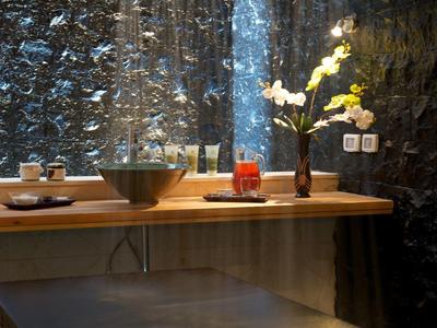 Modern badkamer met regendouches, houten tafel en decoratieve bloemen tegen een donkere muur.