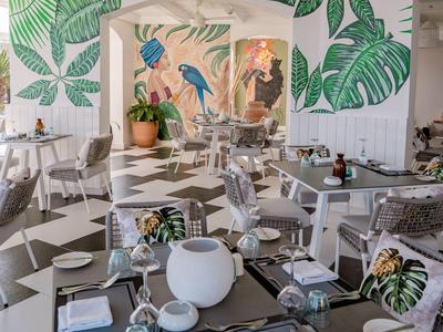 Licht ingericht interieur van een restaurant met tropische bladmotieven op de muren en modern meubilair.