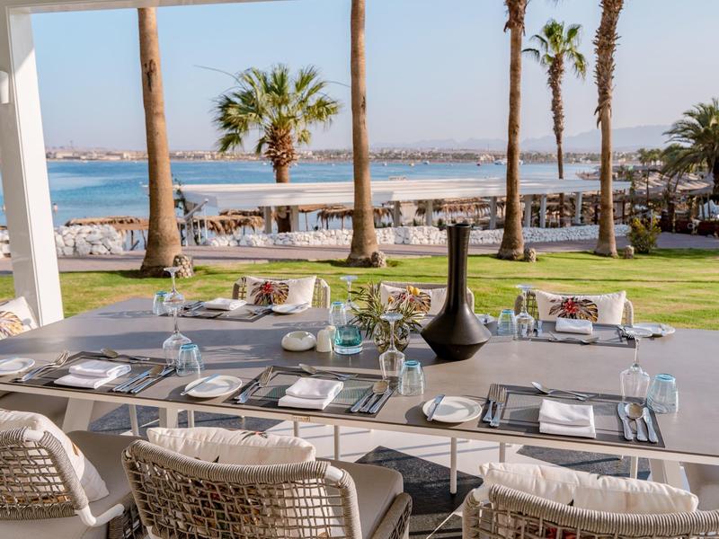 Elegant eetafel met uitzicht op palmbomen en strand bij een hotelrestaurant.