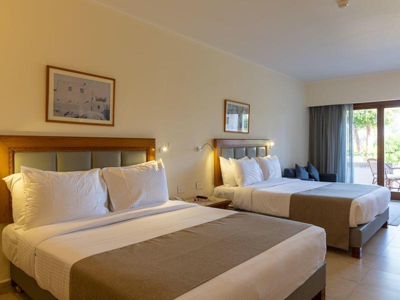 Habitación de hotel luminosa con dos camas dobles y acceso a un balcón.