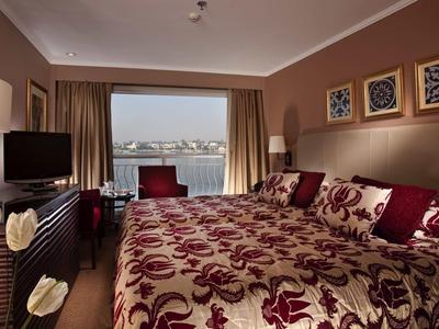 Habitación de hotel acogedora con cama grande, vista al agua desde la ventana y cojines decorativos.