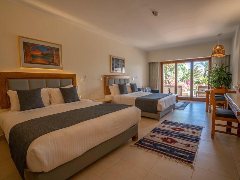 Habitación de hotel luminosa con dos camas, alfombras y balcón con vista al jardín