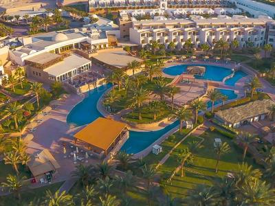 Ośrodek hotelowy z dużymi basenami otoczonymi palmami i zielonym trawnikiem.