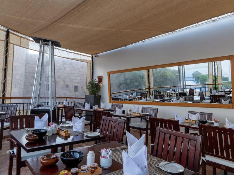 Área de comedor al aire libre con mesas y sillas de madera bajo una sombrilla.