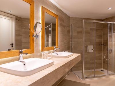 Salle de bain d'hôtel avec deux lavabos, miroirs encadrés en bois et cabine de douche en verre.