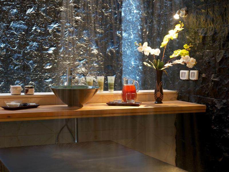 Salle de bain moderne avec douches à effet pluie, table en bois et fleurs décoratives devant un mur sombre.