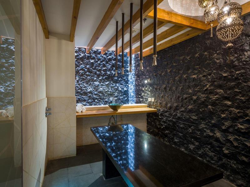 Salle de massage avec table noire et murs en pierre éclairés doucement.