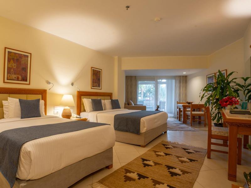 Chambre d'hôtel confortable avec deux lits, bureau, plantes et accès à un balcon.