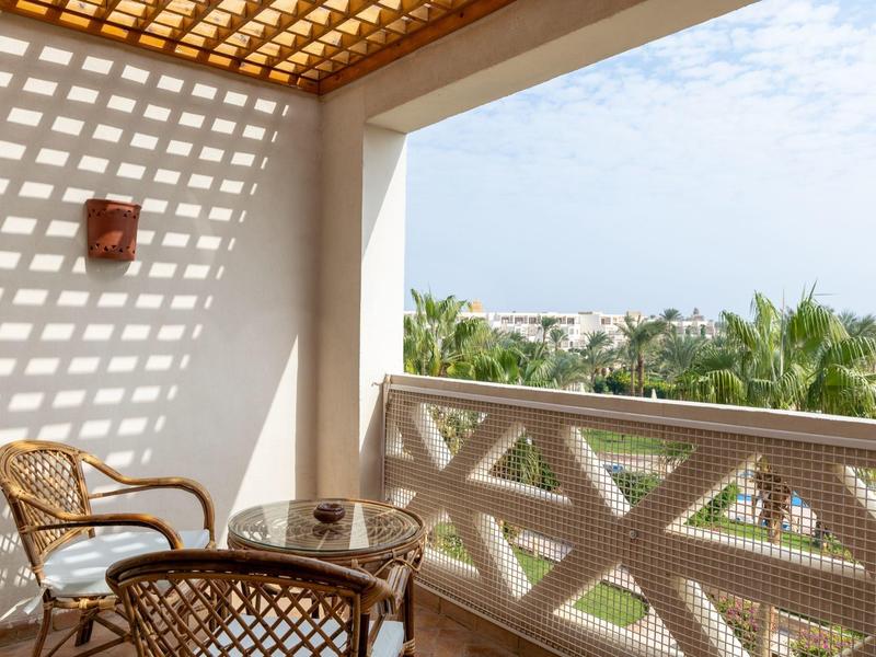 Balcon avec chaises en osier et table, vue sur les palmiers et le ciel.