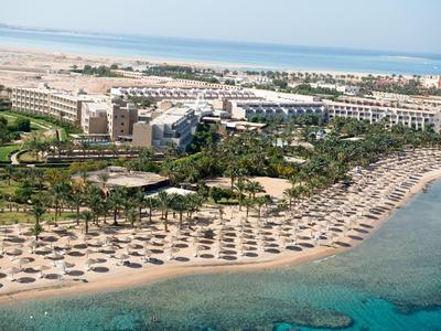 Luchtfoto van een groot resort aan het strand met parasols en ligbedden langs het zand, dichtbij helder blauw water.