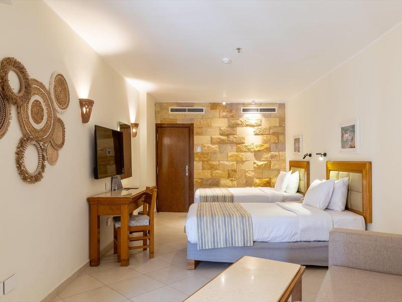 Lichte hotelkamer met twee bedden, flatscreen-tv, bureau en decoratieve wandstukken van riet.