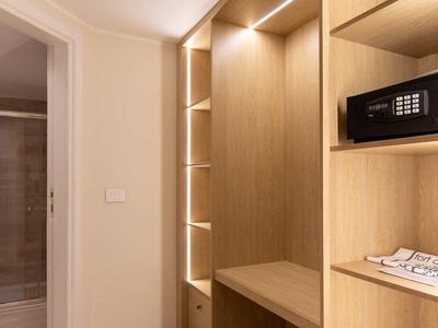 A walk-in closet with built-in safe and illuminated wooden shelves next to a bathroom.