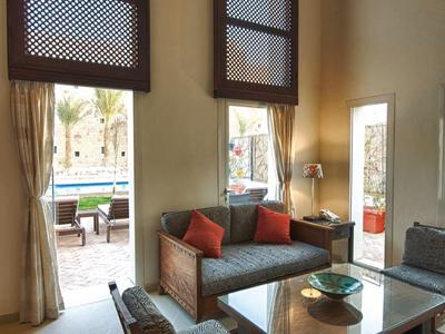 Bright hotel lounge with tall windows, seating, and rug in front of terrace with pool