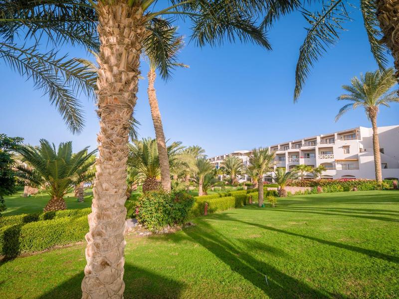 Hotel building with well-maintained garden and palm trees under clear blue sky.