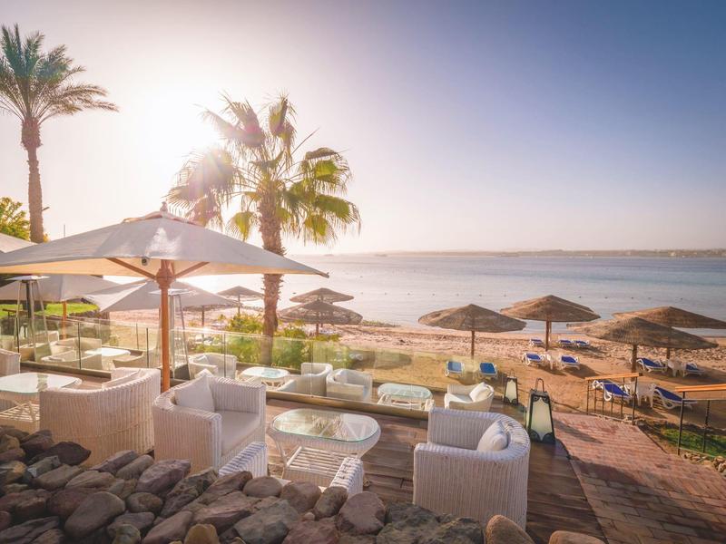 Lounge area with seating and umbrellas on the beach at sunset.