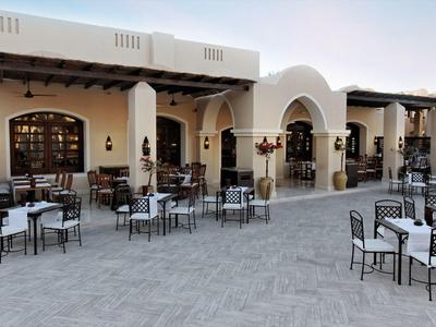 Hotel outdoor area with multiple tables and chairs on a paved terrace under arches.