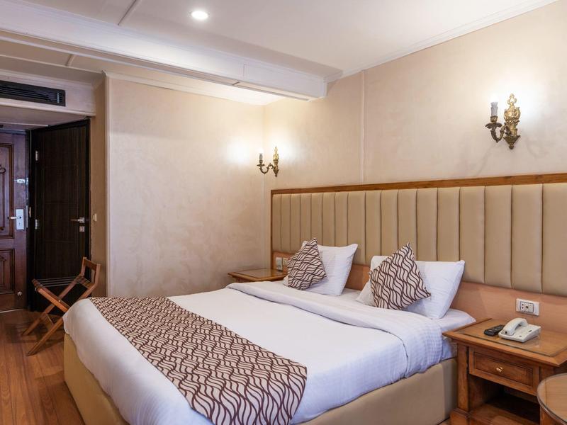 Cozy hotel room with double bed, wooden floor, bedside table, and soft lighting.