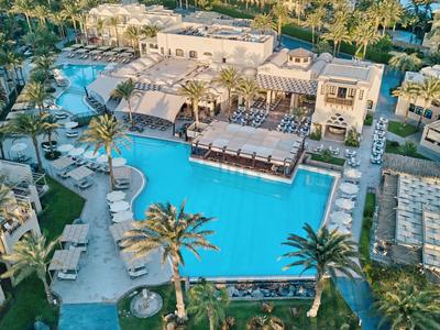 Vue aérienne d'une grande piscine d'hôtel avec palmiers et chaises longues.