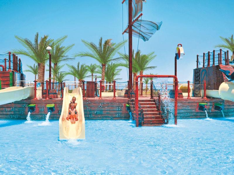 Parque acuático con toboganes de agua, palmeras y agua clara azul bajo un cielo soleado.