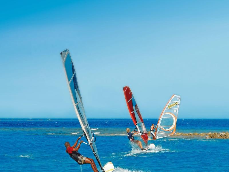 Drie windsurfers glijden over helderblauwe zee op een zonnige dag.