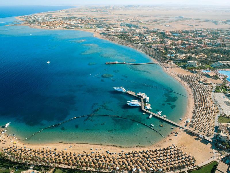 Coastline with sandy beach, sun loungers, a long wooden pier, and clear blue water.
