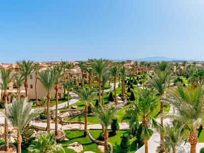Vue panoramique d'un complexe hôtelier avec piscines, palmiers et bâtiments sable sous un ciel clair.