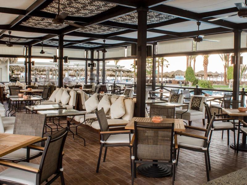 Terrasse de restaurant spacieuse avec tables et chaises en bois, vue sur la mer au coucher du soleil.