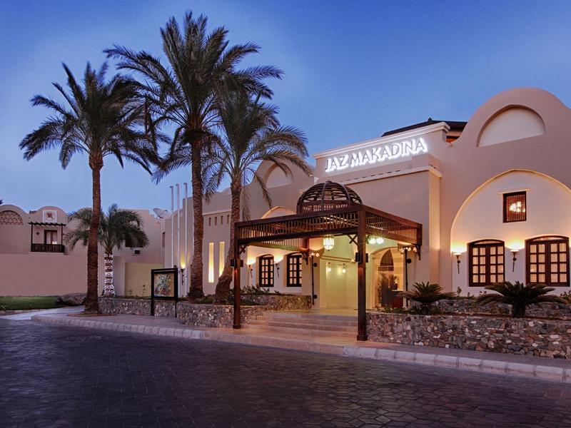 Ingresso illuminato di un hotel in stile mediterraneo con palme al crepuscolo.