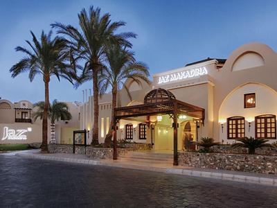 Illuminated hotel entrance with white facade and palm garden at dusk.