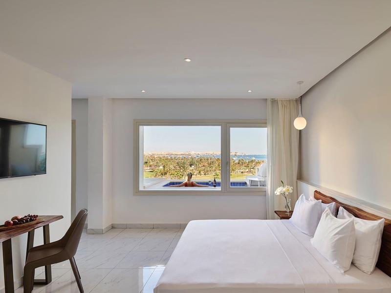 Camera d'hotel moderna con letto grande, scrivania, TV e finestra con vista sulla città.