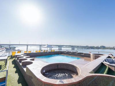 Piscine ronde et bains à remous sur une terrasse ensoleillée avec vue sur la rivière.