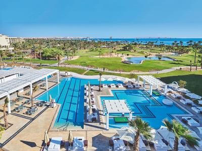 Gran piscina exterior con tumbonas con vistas al campo de golf y al mar bajo un cielo claro y soleado.