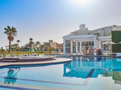 Piscina exterior moderna con terraza soleada y palmeras bajo un cielo despejado.
