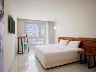 Modern hotelkamer met groot tweepersoonsbed, houten hoofdeinde en raam met uitzicht naar buiten.